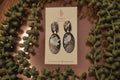 Pair of earrings on a branded card with decorative greenery around
