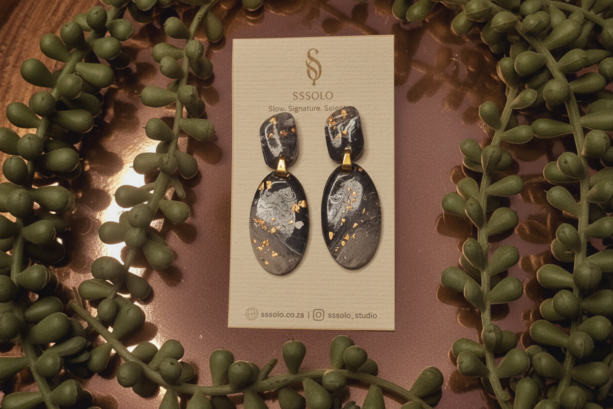 Pair of earrings on a branded card with decorative greenery around