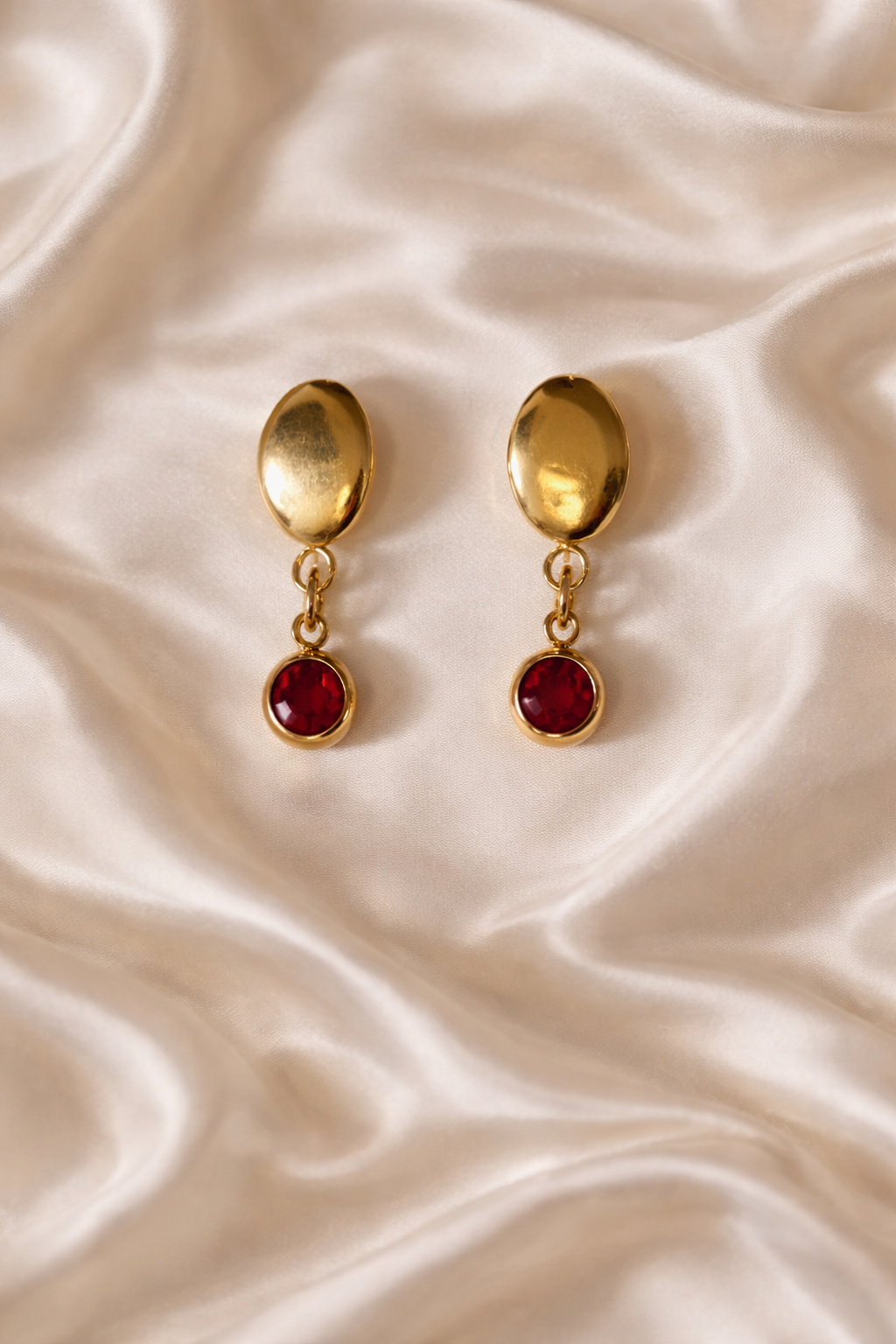 Gold earrings with red gemstones on a beige fabric background