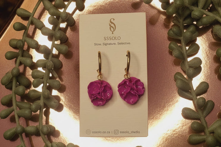 Pair of pink earrings on a branded card with a decorative background