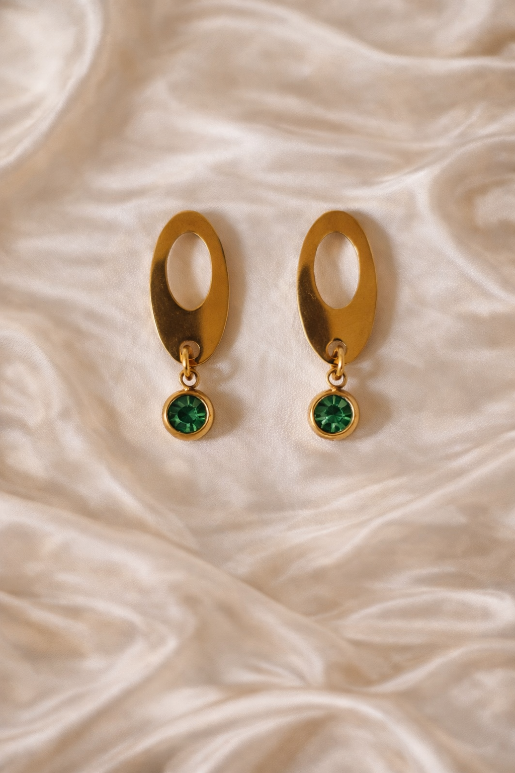 Gold earrings with green gemstones on a beige fabric background