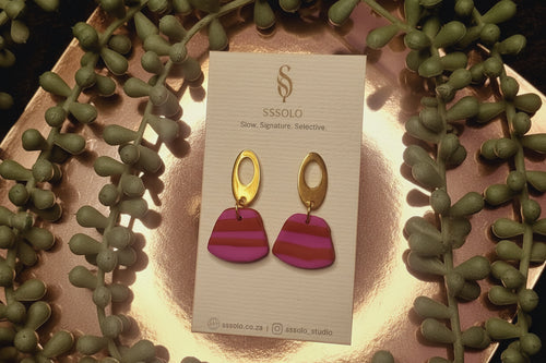 Pair of pink and red gold detail earrings on a Ssolo branded card with green leaves in the background