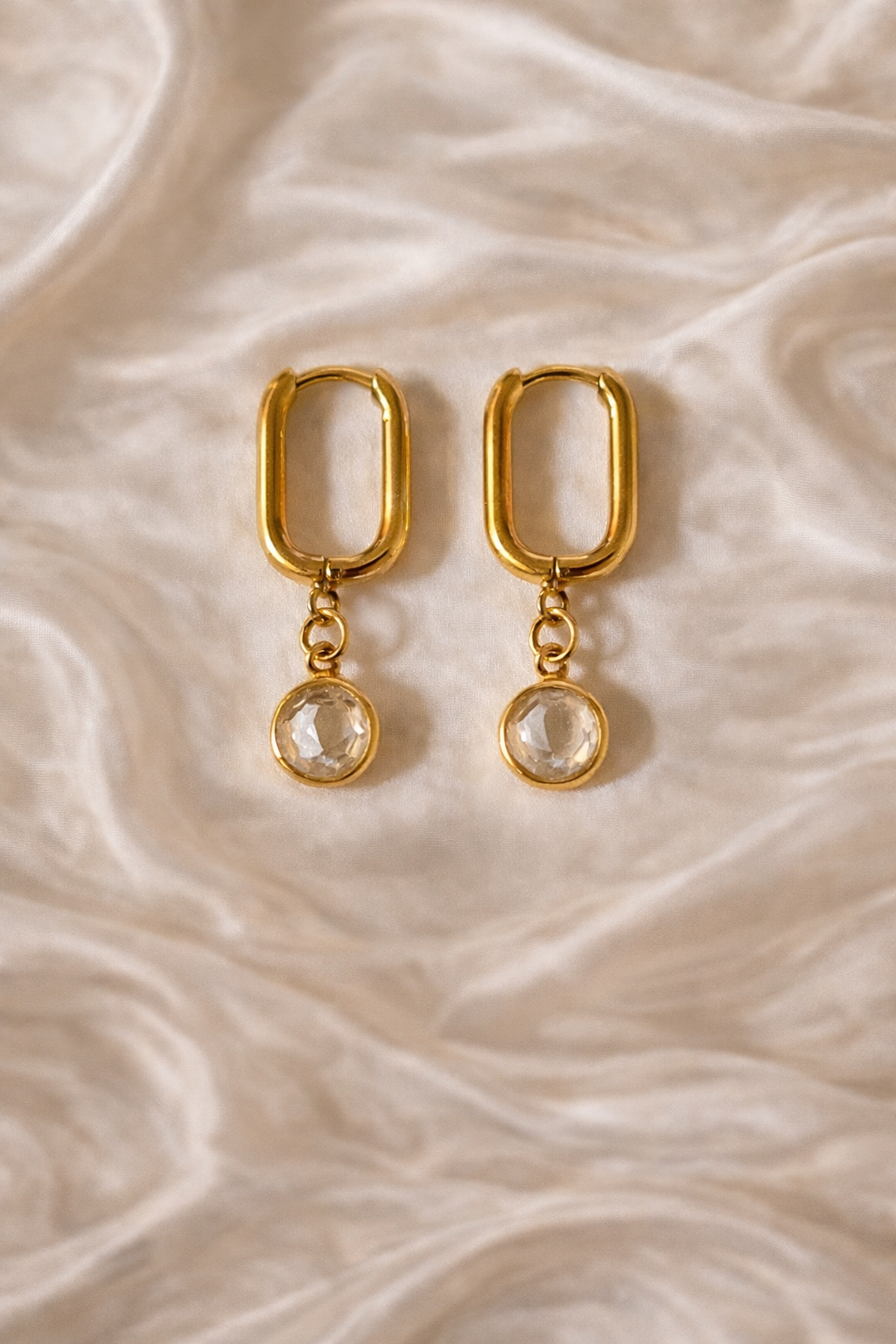 Gold hoop earrings with clear gemstones on a beige marble background